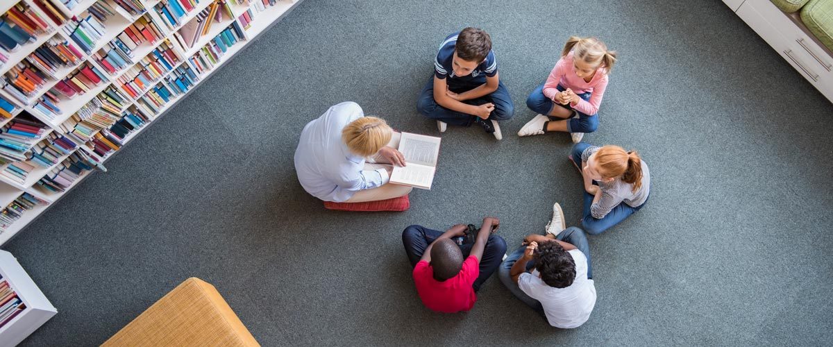 teacher and students reading on floor in library